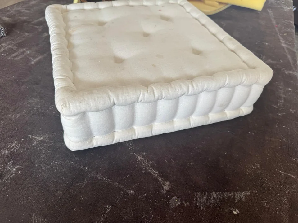 Cream rectangular upholstered cushion with button tufting and a gathered edge
