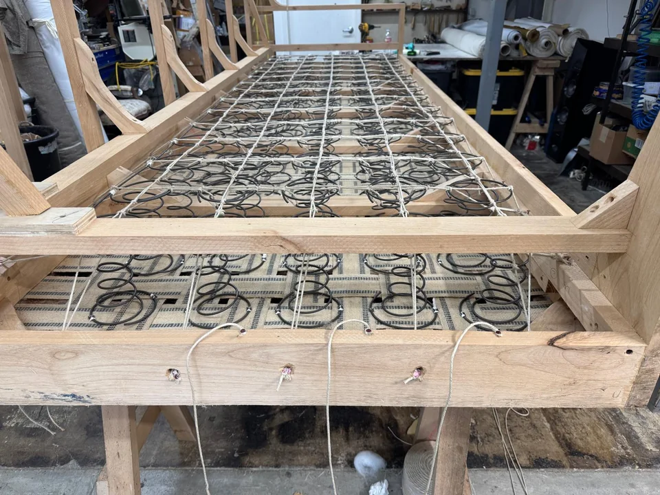 Long wooden furniture frame showing rows of tied springs from one end
