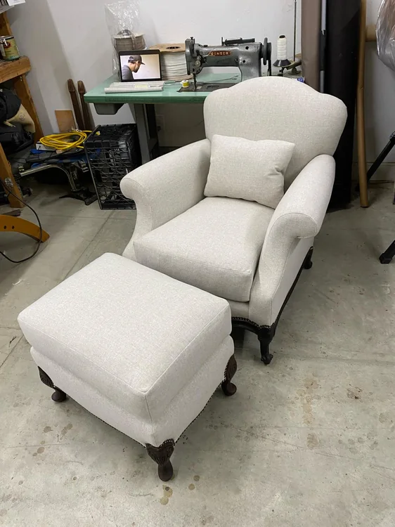 Cream upholstered armchair with a matching cushion and ottoman in the workshop