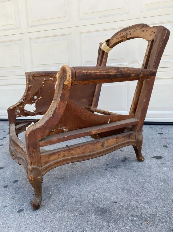 Bare wooden armchair frame with curved legs and remnants of the original upholstery