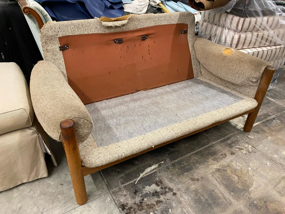 Wood-framed loveseat with worn beige upholstery and its seat and back cushions removed