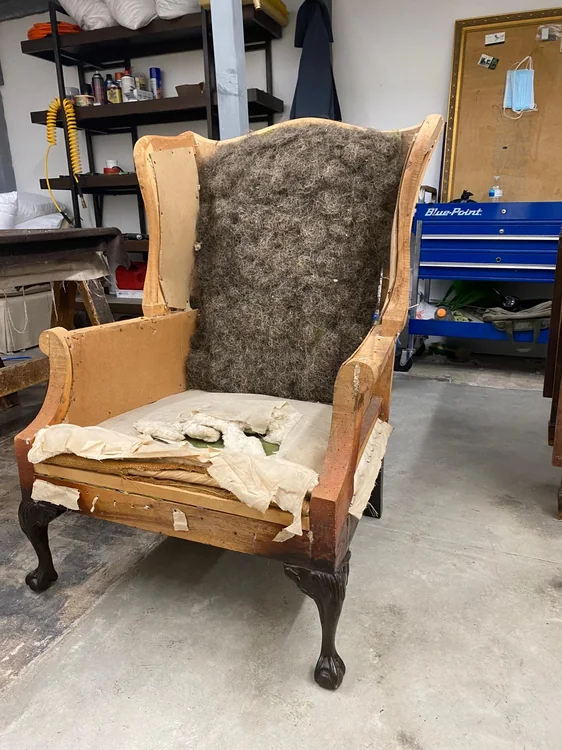 Wingback chair stripped to its wooden frame with exposed back padding and torn seat fabric