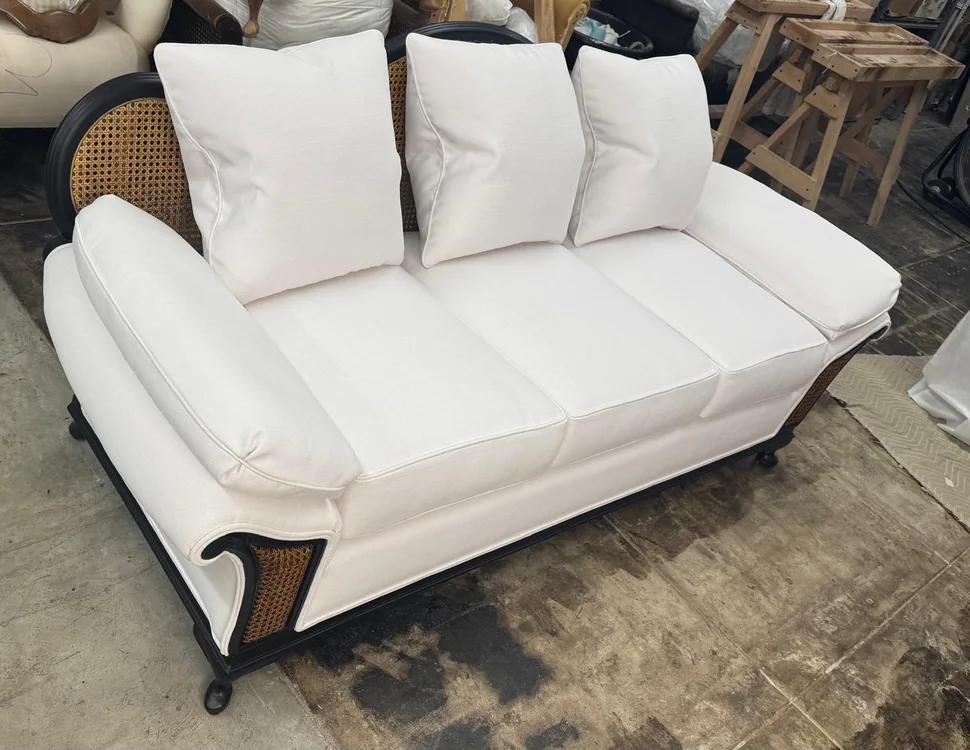 Cane-back sofa with cream upholstery, three back cushions, and a dark wood frame