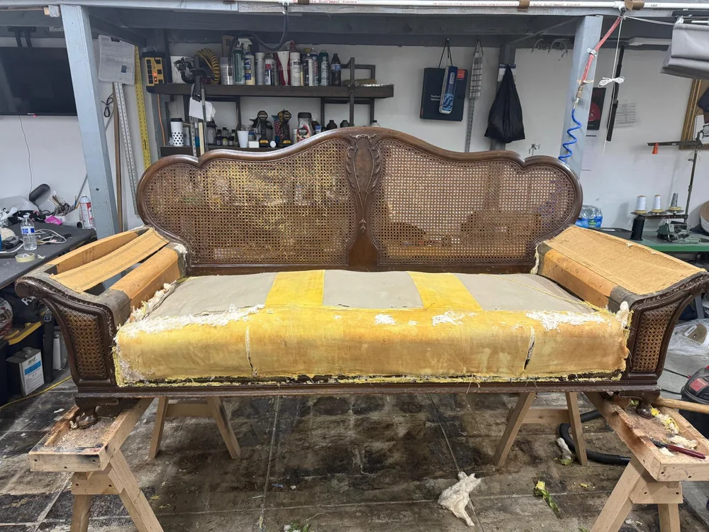 Carved wooden cane-back sofa with exposed yellow seat padding and stripped arms
